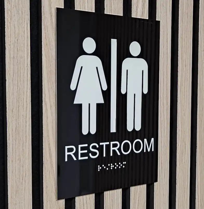 Sort toiletskilt, med hvid skrift og braile
