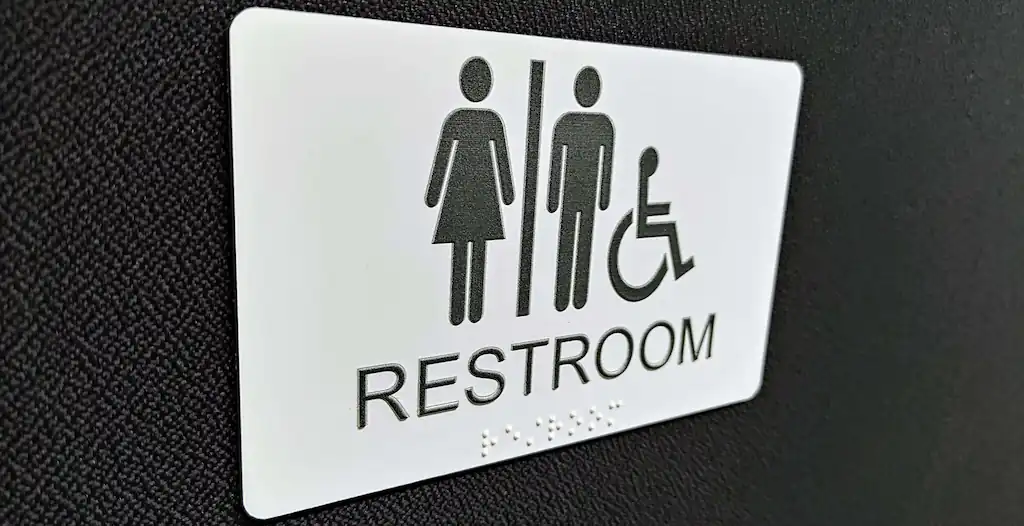 Hvidt toiletskilt, med sort skrift og braile